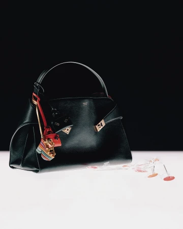 Black leather handbag with decorative charms resting on a white surface against a contrasting black background for Ferragamo