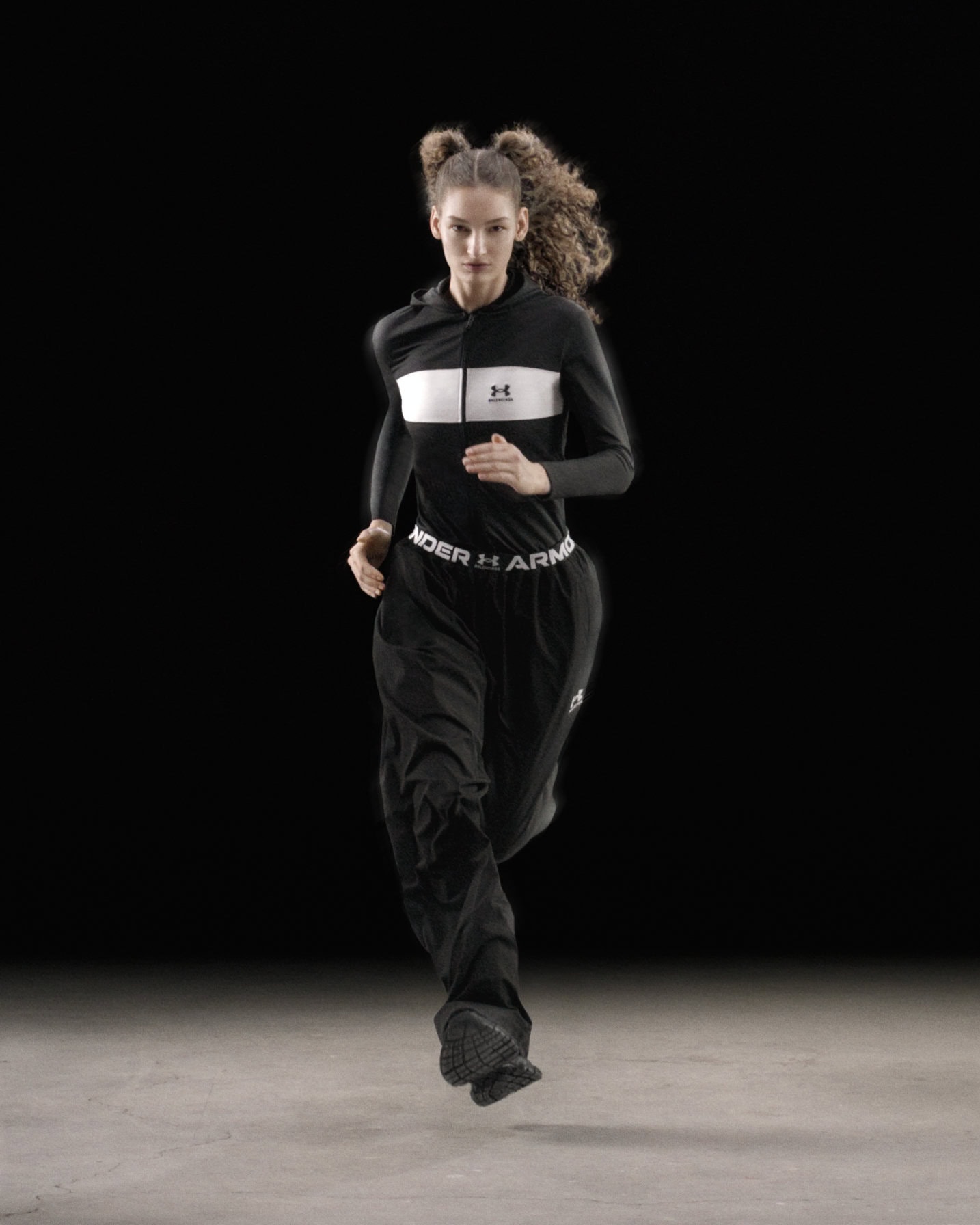 Female athlete running in black sportswear against a dark studio background