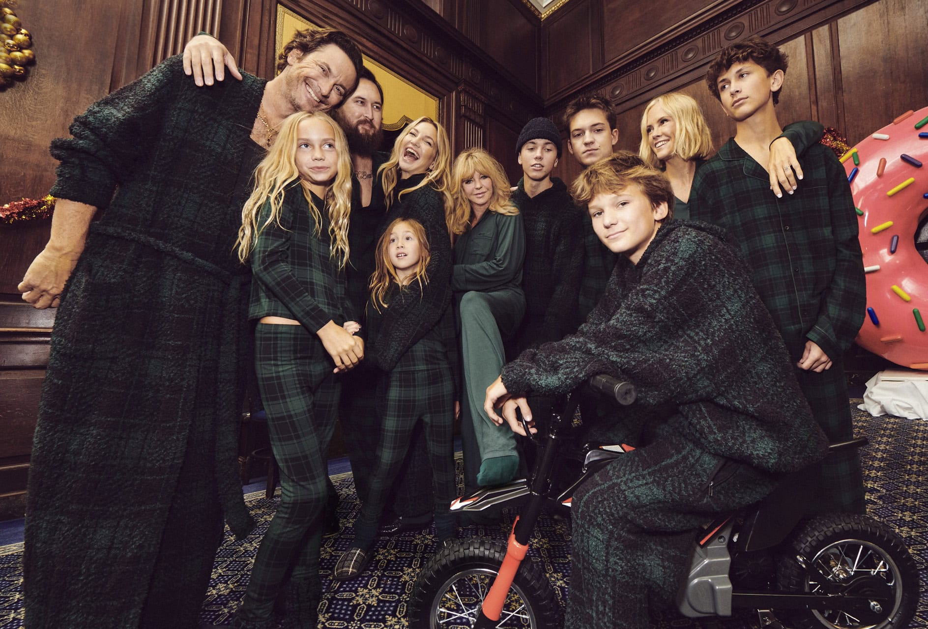Group portrait of a family wearing dark green plaid loungewear in a wood-paneled room for SKIMS Holiday 2024 campaign