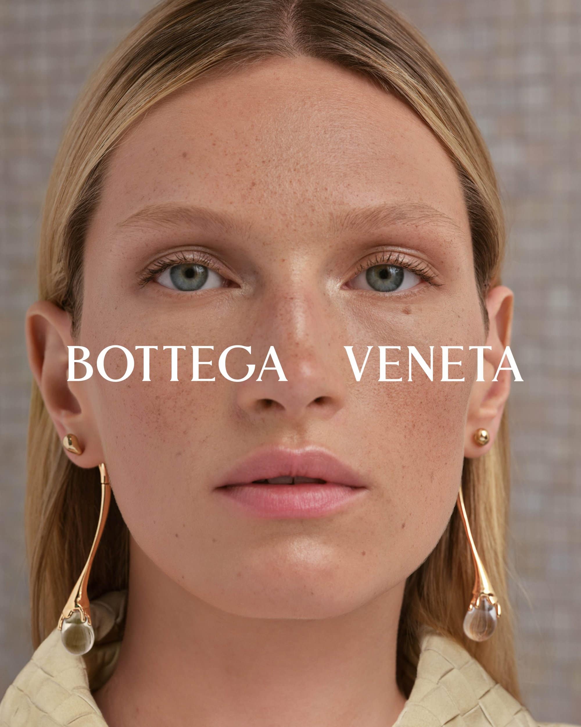 Close-up portrait of a woman wearing long gold drop earrings and a pale textured top for Bottega Veneta Winter Solstice 2024