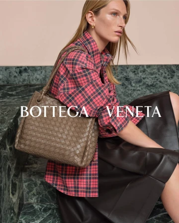 Model wearing a pink plaid shirt and dark leather skirt holding a woven leather handbag against a green marble surface.