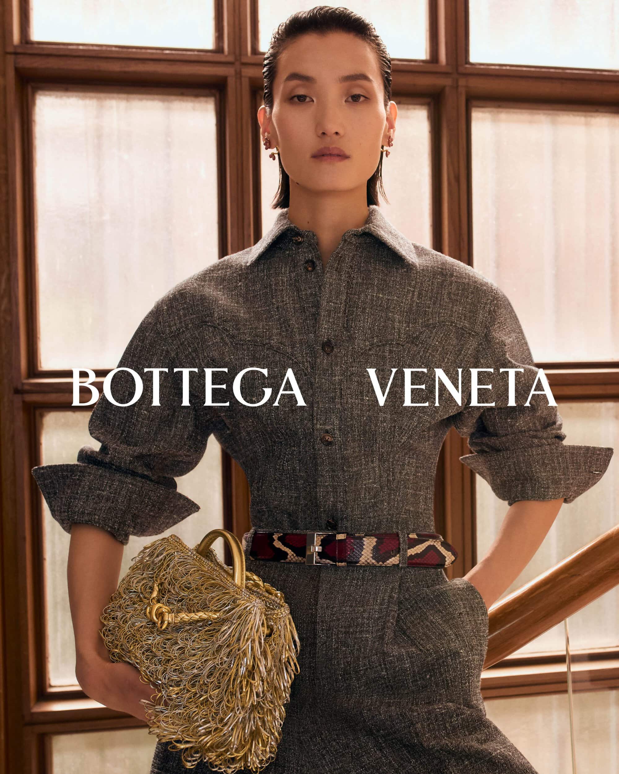 Model in grey tweed shirt dress holding a textured gold fringed handbag by Bottega Veneta