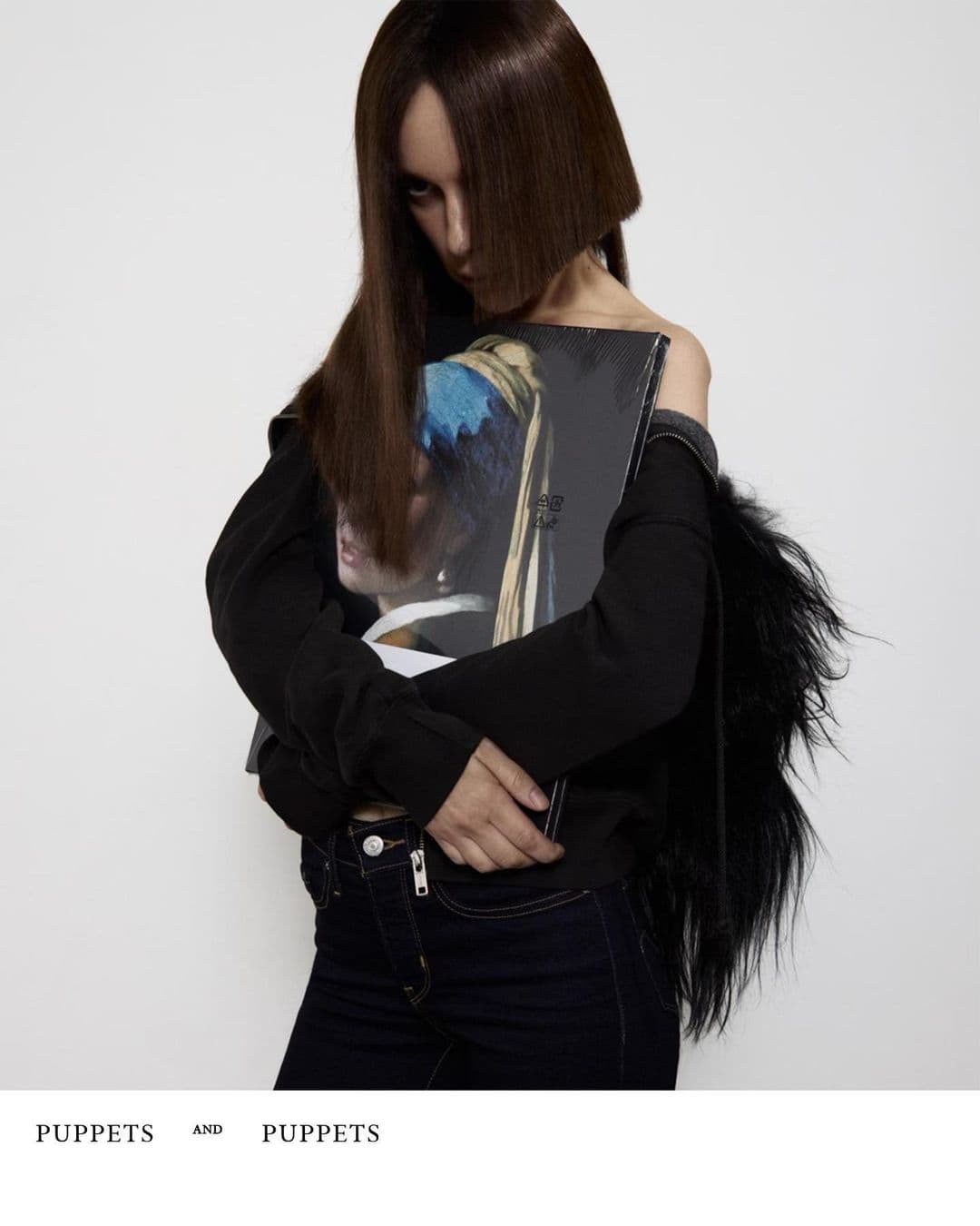 Model holding a framed artwork featuring a classic painting against a plain background for Puppets and Puppets