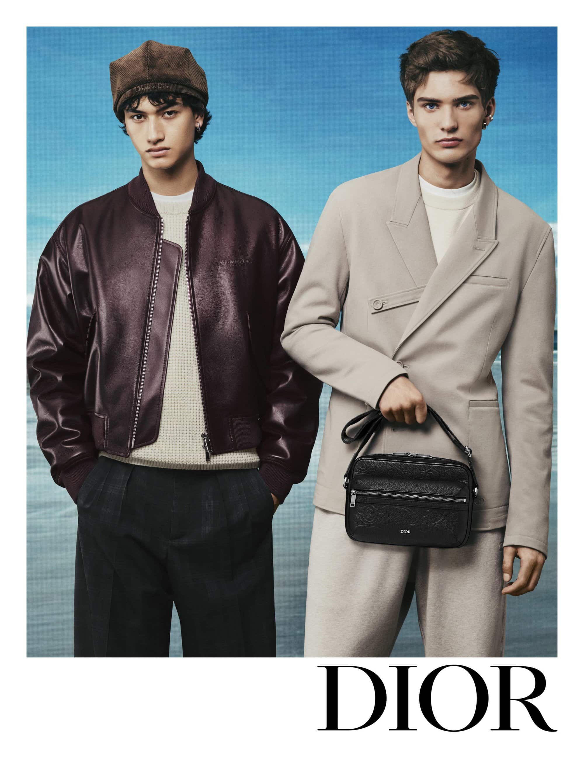 Two male models posing against a painted blue sky backdrop for Dior Men's Spring 2025 ad campaign, wearing structured jackets and trousers.