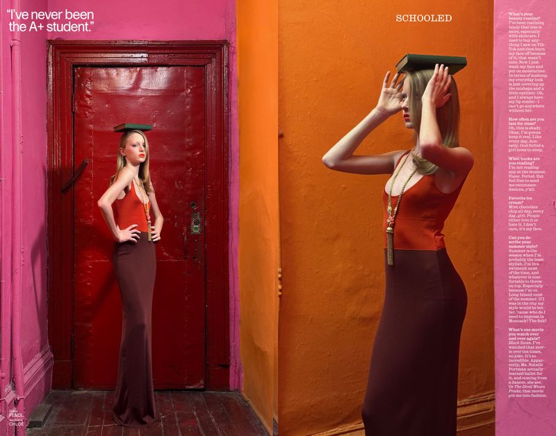 Fashion editorial shot of a woman posing with a book on her head, wearing a red top and maroon skirt against vibrant orange and pink walls.