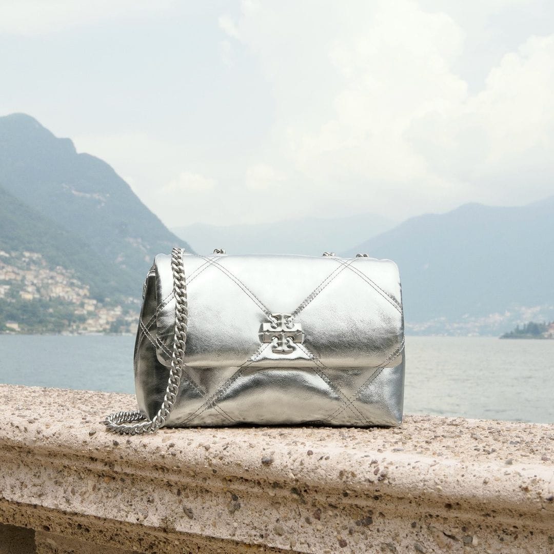 Metallic silver quilted shoulder bag with chain strap resting on a stone ledge overlooking Lake Como