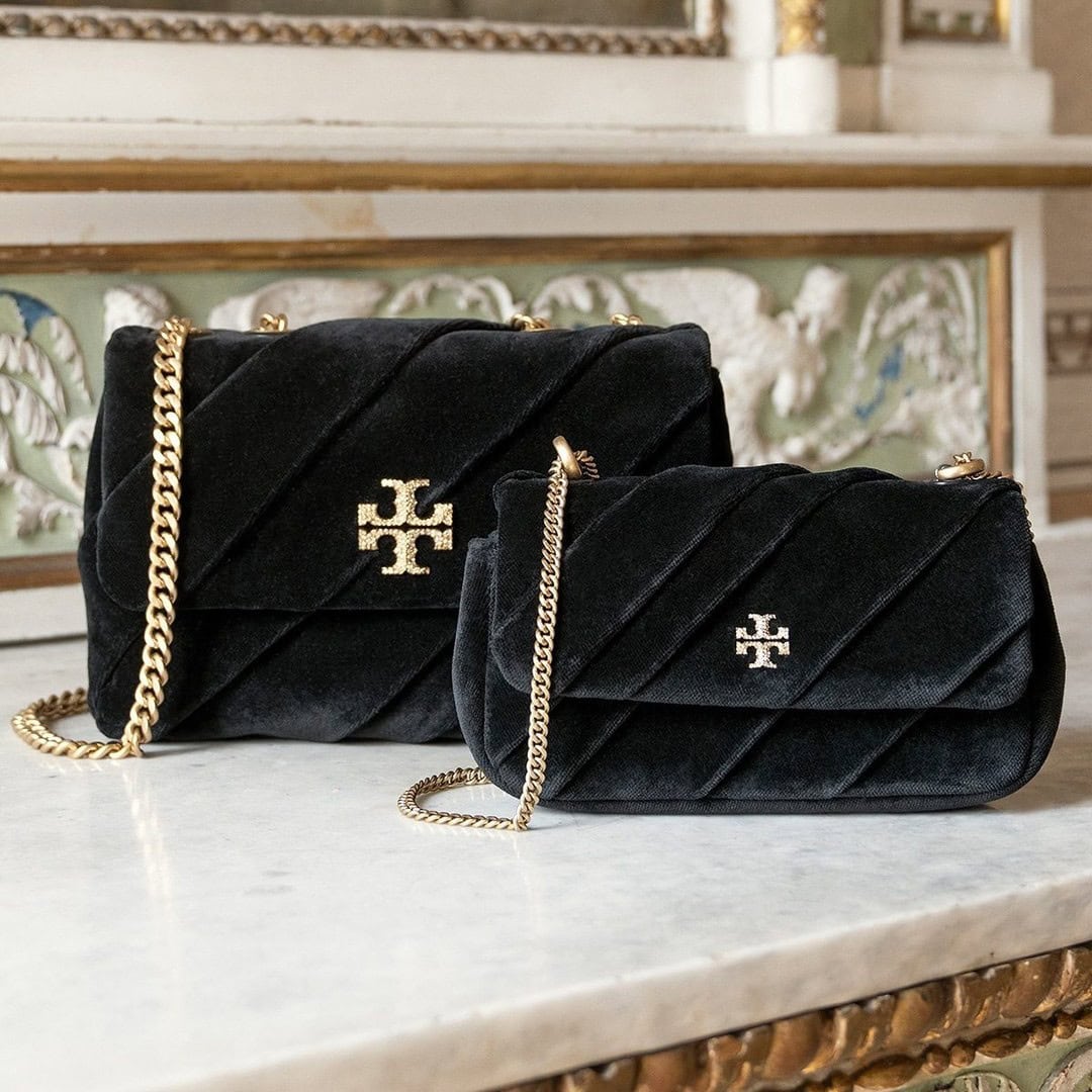 Two black quilted velvet handbags with gold chain straps resting on a white marble surface.