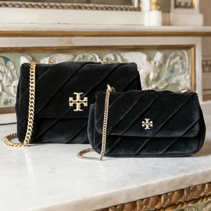 Two black quilted velvet handbags with gold chain straps resting on a white marble surface.