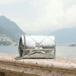Metallic silver quilted shoulder bag with chain strap resting on a stone ledge overlooking Lake Como