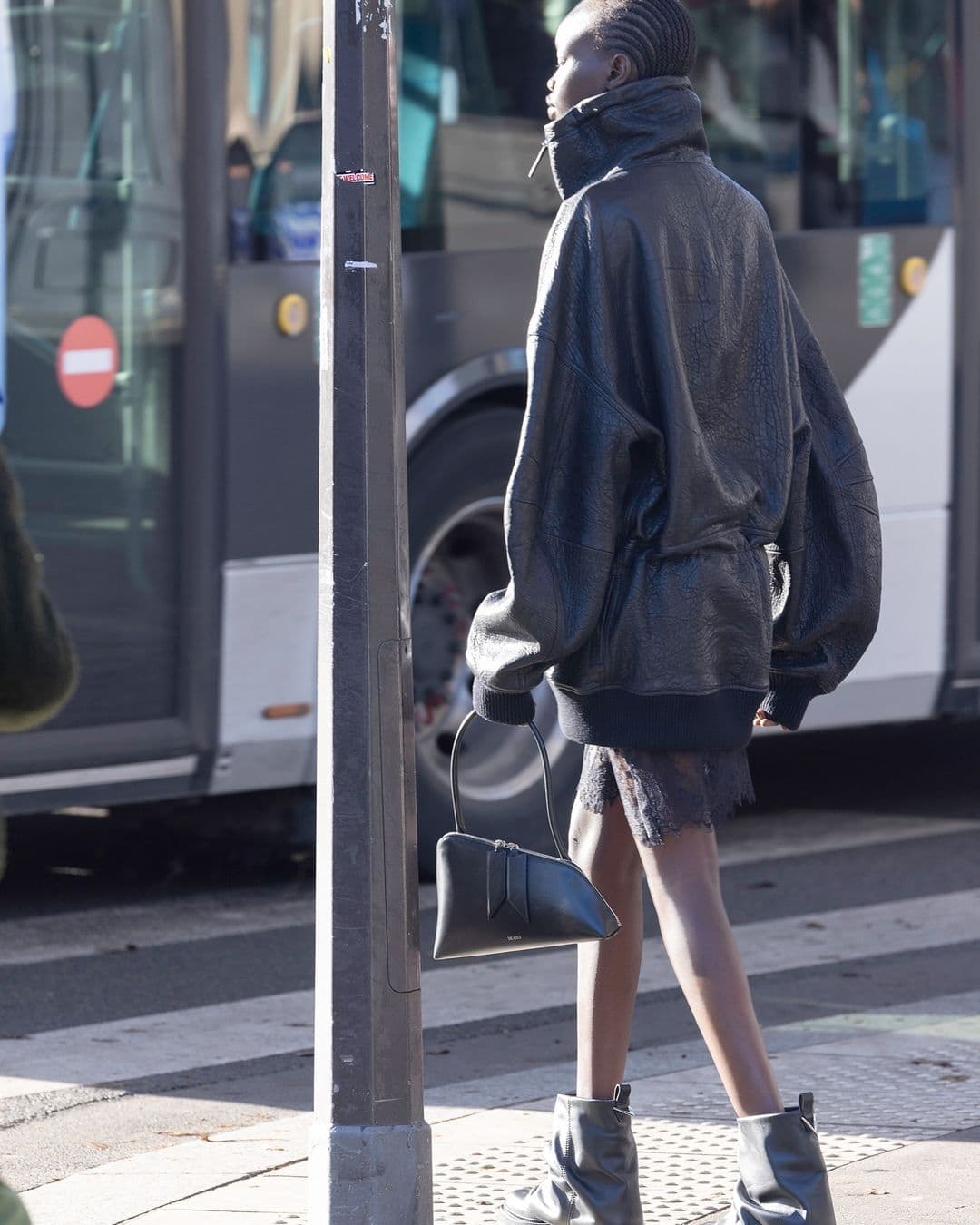 Model in black leather jacket and boots walking on city street holding a handbag
