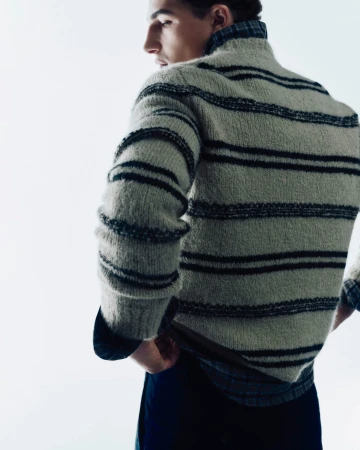 Man wearing a textured striped sweater over a plaid shirt against a bright white seamless background