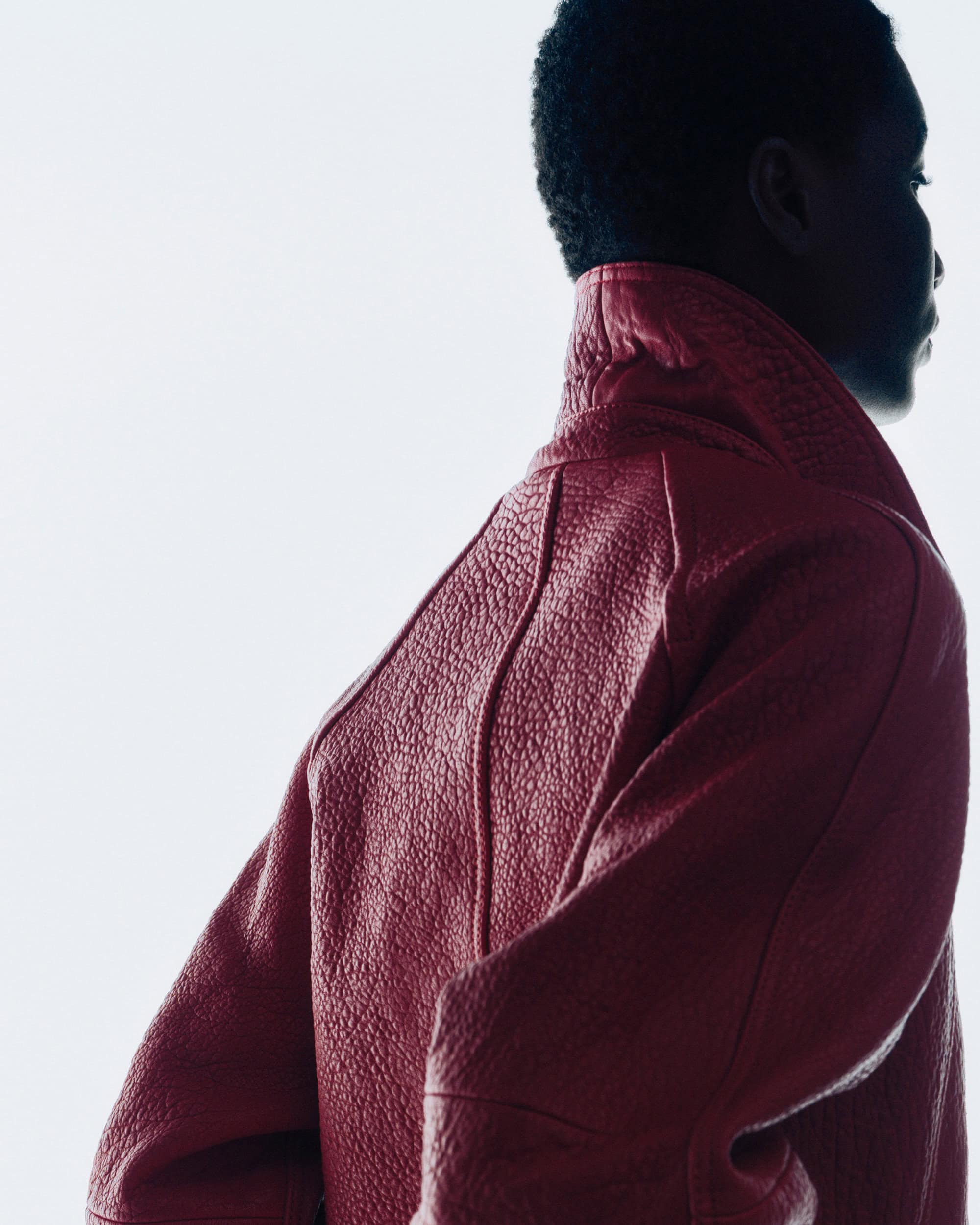 Close-up profile of a model wearing a textured red leather jacket against a bright white background.