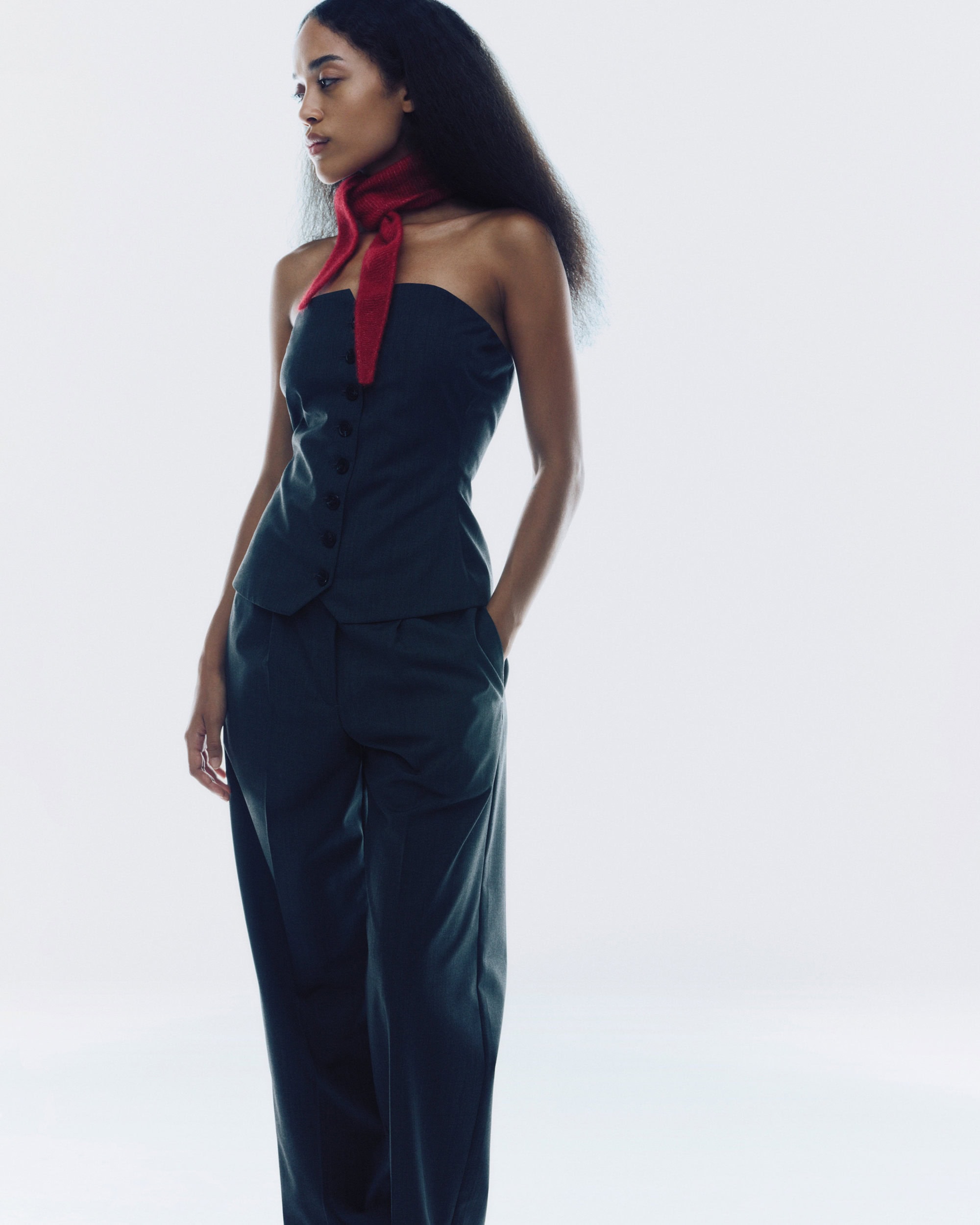 Model wearing a dark strapless top, matching trousers, and a bright red scarf against a plain white background.