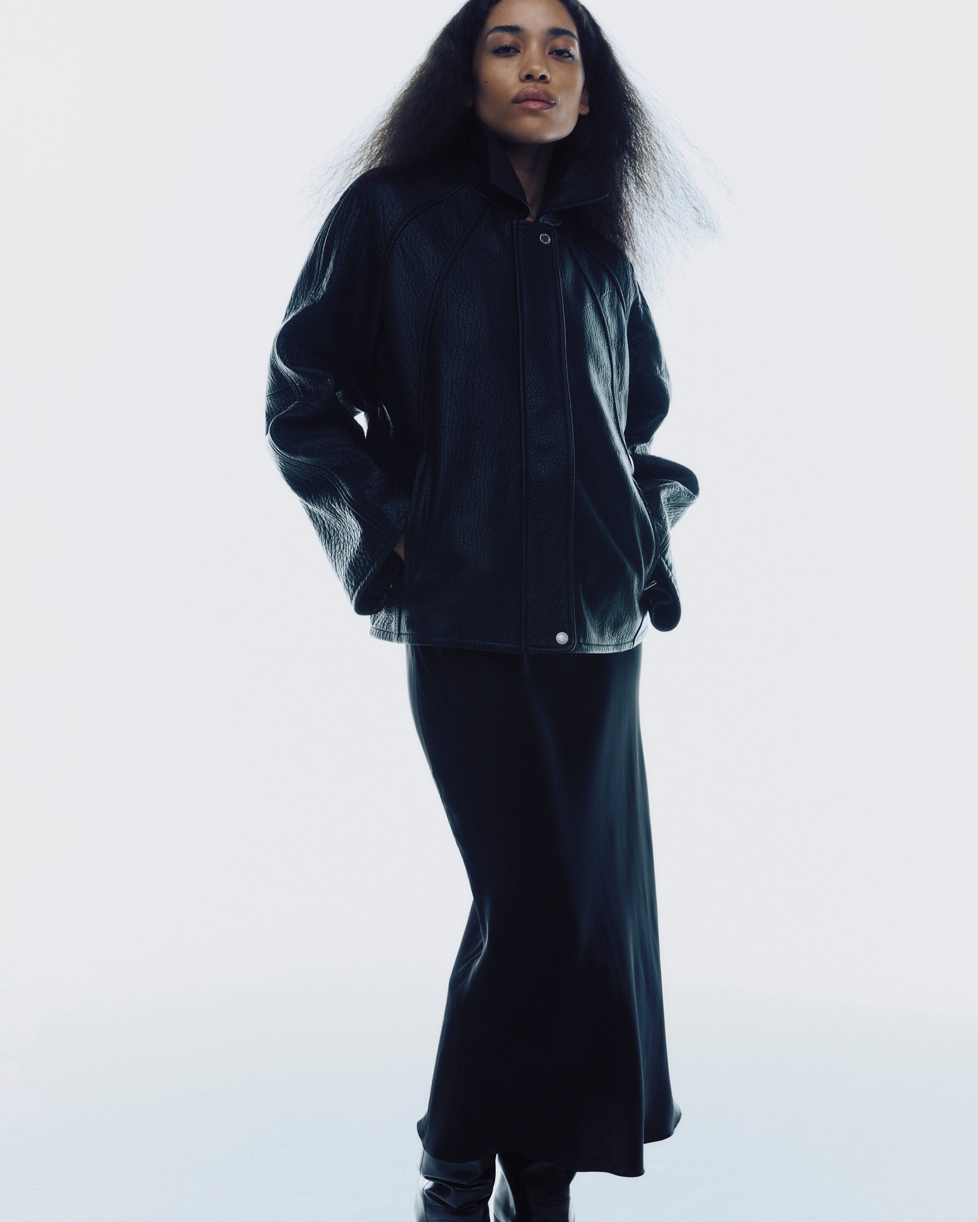 Model wearing a black leather jacket and long black skirt against a white studio background for Samsoe Samsoe.