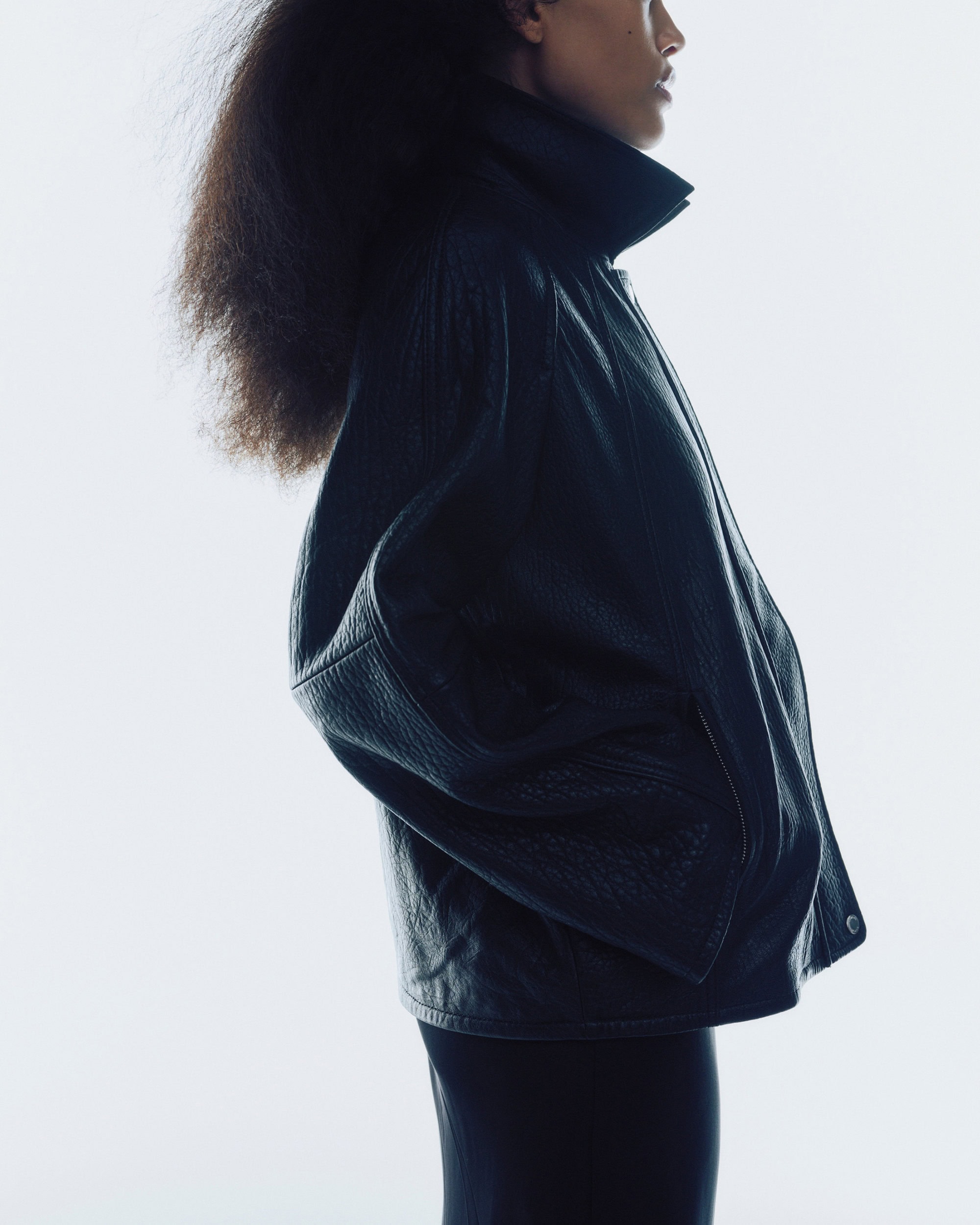Profile view of a model wearing a dark leather jacket against a white background