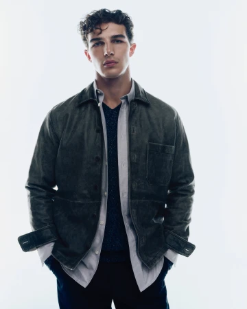 A man wearing a dark olive jacket and open grey shirt against a plain white background for Samsøe Samsøe pre-spring 2025 ad campaign.