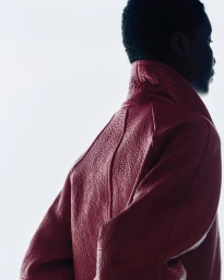 Close-up profile of a model wearing a textured red leather jacket against a bright white background.