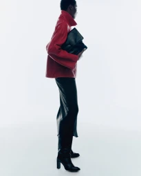 Model in red leather jacket and black skirt holding a black clutch against a white background