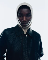 Model wearing a white ribbed knit balaclava and dark leather jacket against a bright white background for Samsoe Samsoe campaign