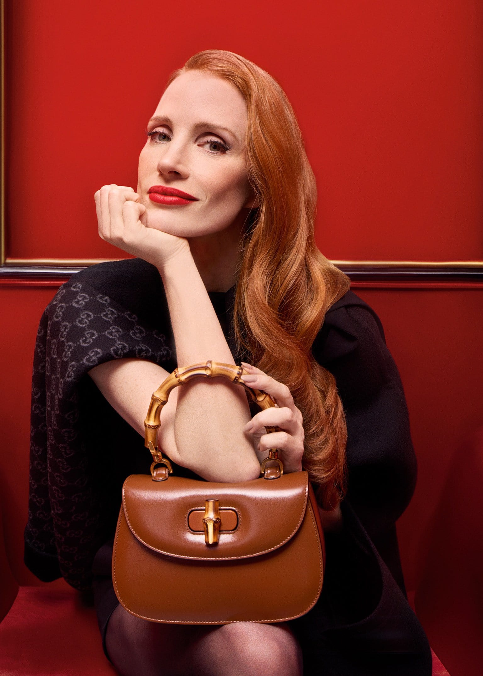 Jessica Chastain posing with a brown leather Gucci bamboo handle bag against a rich red background
