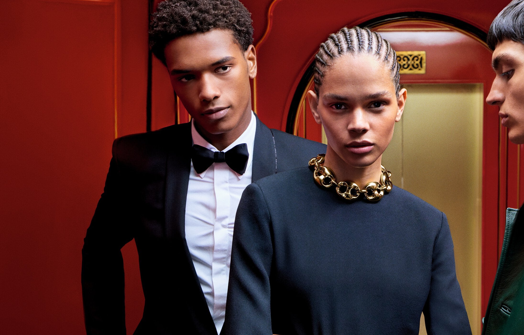 Group of three models in formal attire and heavy gold necklace against a vibrant red background for Gucci Holiday 2024 campaign