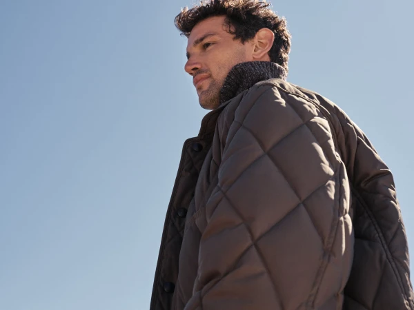 Man wearing a quilted brown jacket against a clear blue sky background