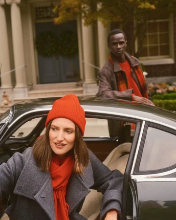 Woman in grey coat and red beanie stepping out of a dark car, with a man standing behind in San Francisco.