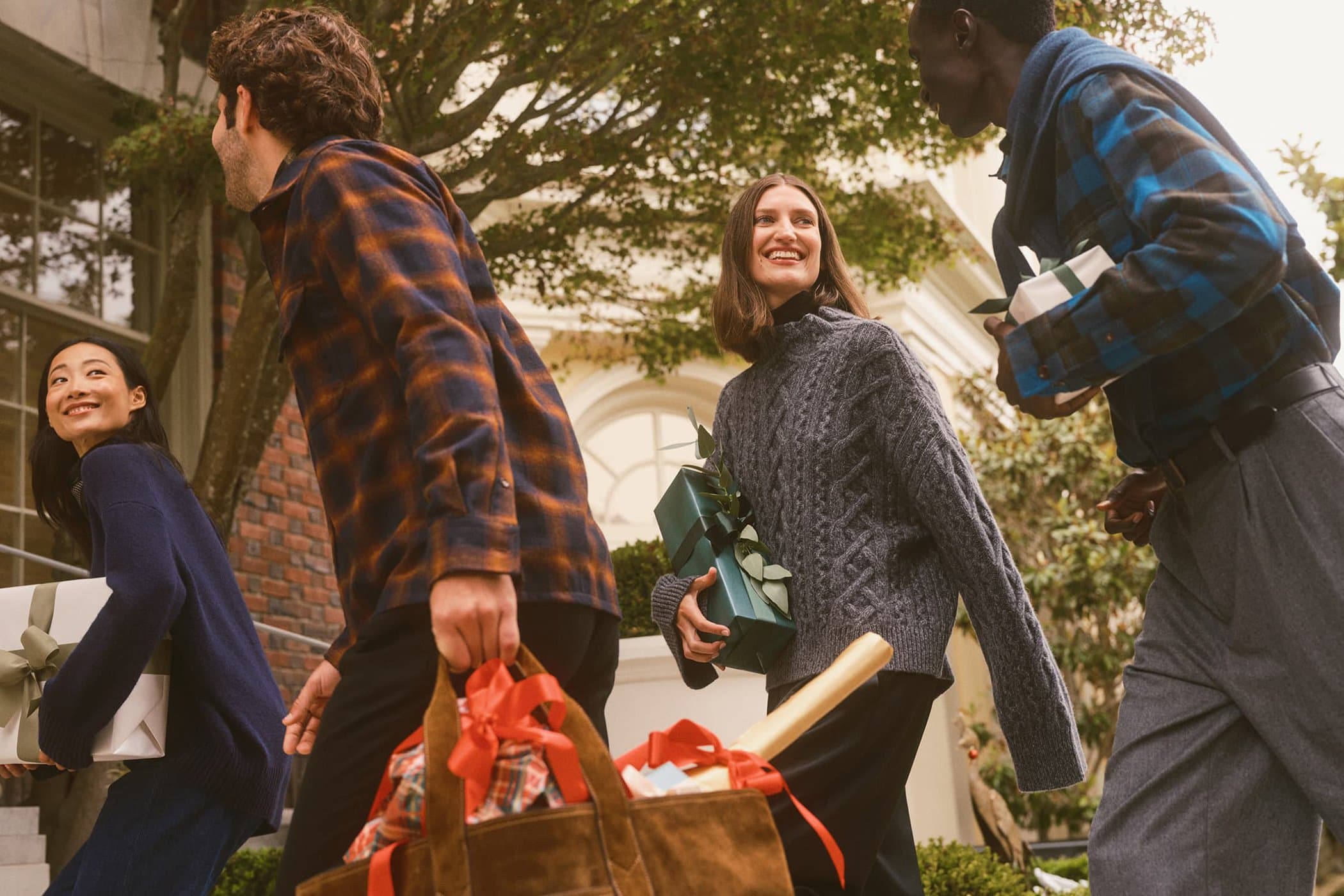 A group of diverse models carrying wrapped gifts and bags outdoors near a building exterior for Banana Republic Holiday 2024 ad campaign.