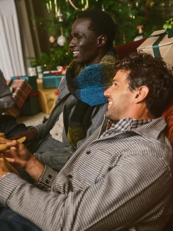 Two smiling men in winter clothing gathered indoors near wrapped holiday gifts for Banana Republic