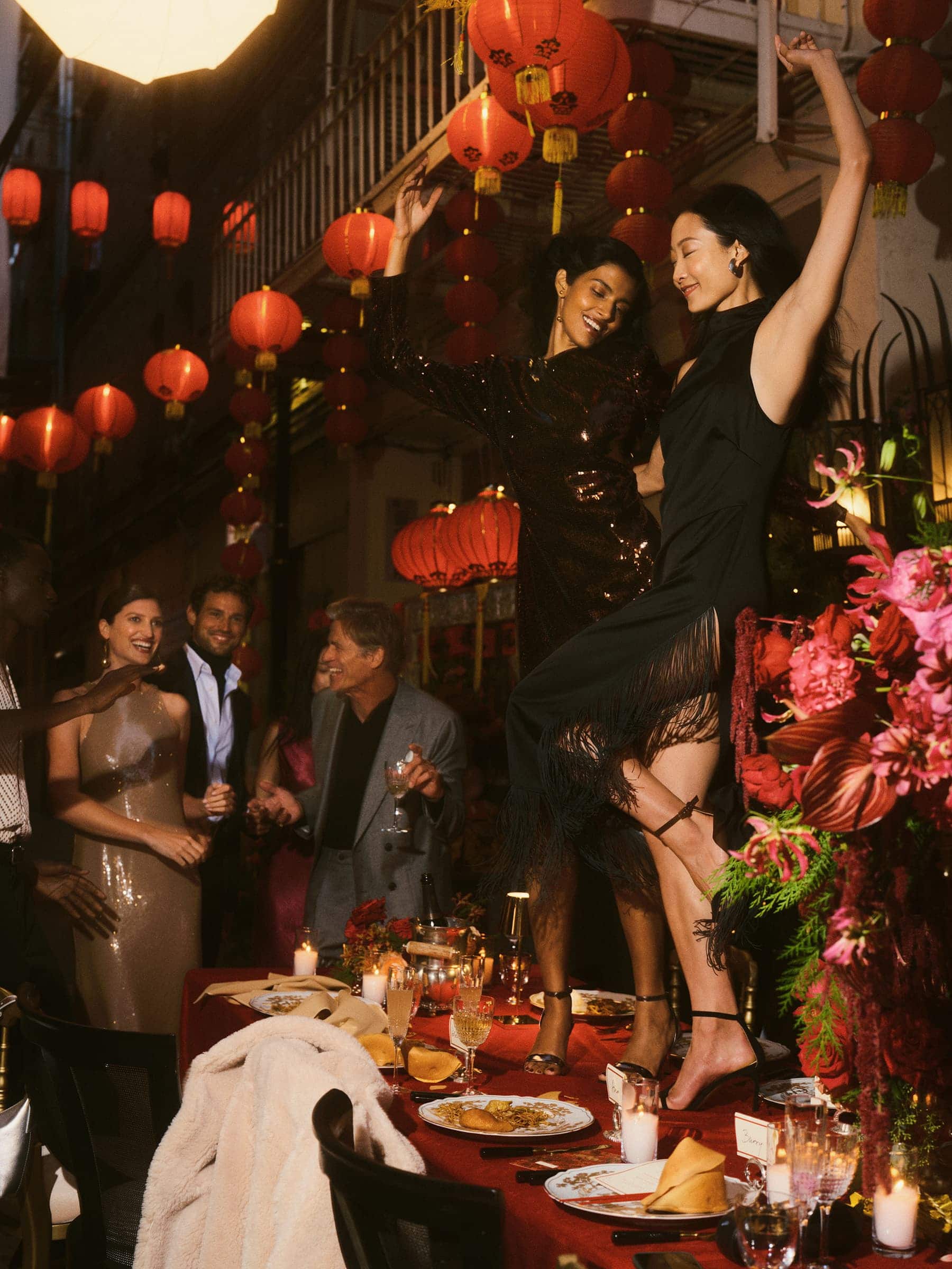 Group of people celebrating around a banquet table decorated with red lanterns and floral arrangements.