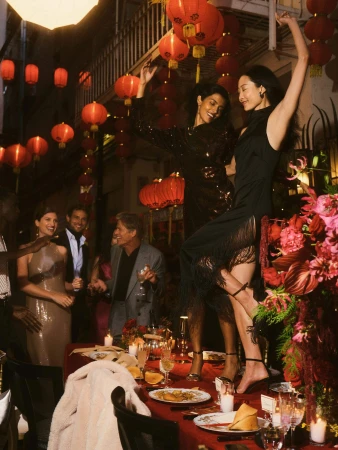 Group of people celebrating around a banquet table decorated with red lanterns and floral arrangements.