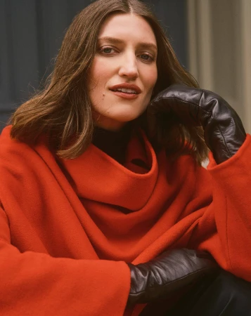 Woman wearing a bright orange coat and black leather gloves against a neutral background