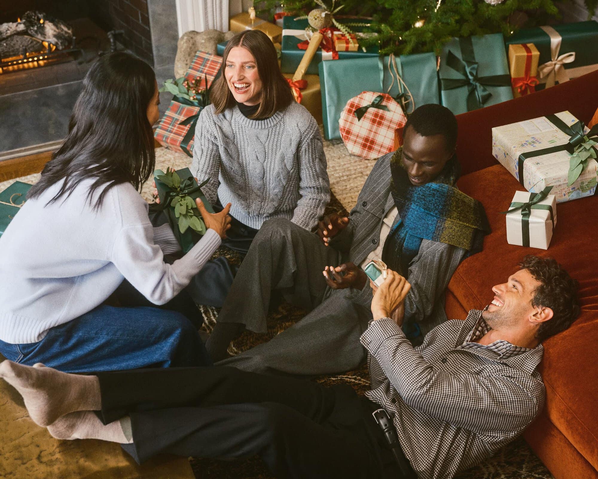 Group of friends opening Christmas gifts together in a cozy living room decorated for the holiday season
