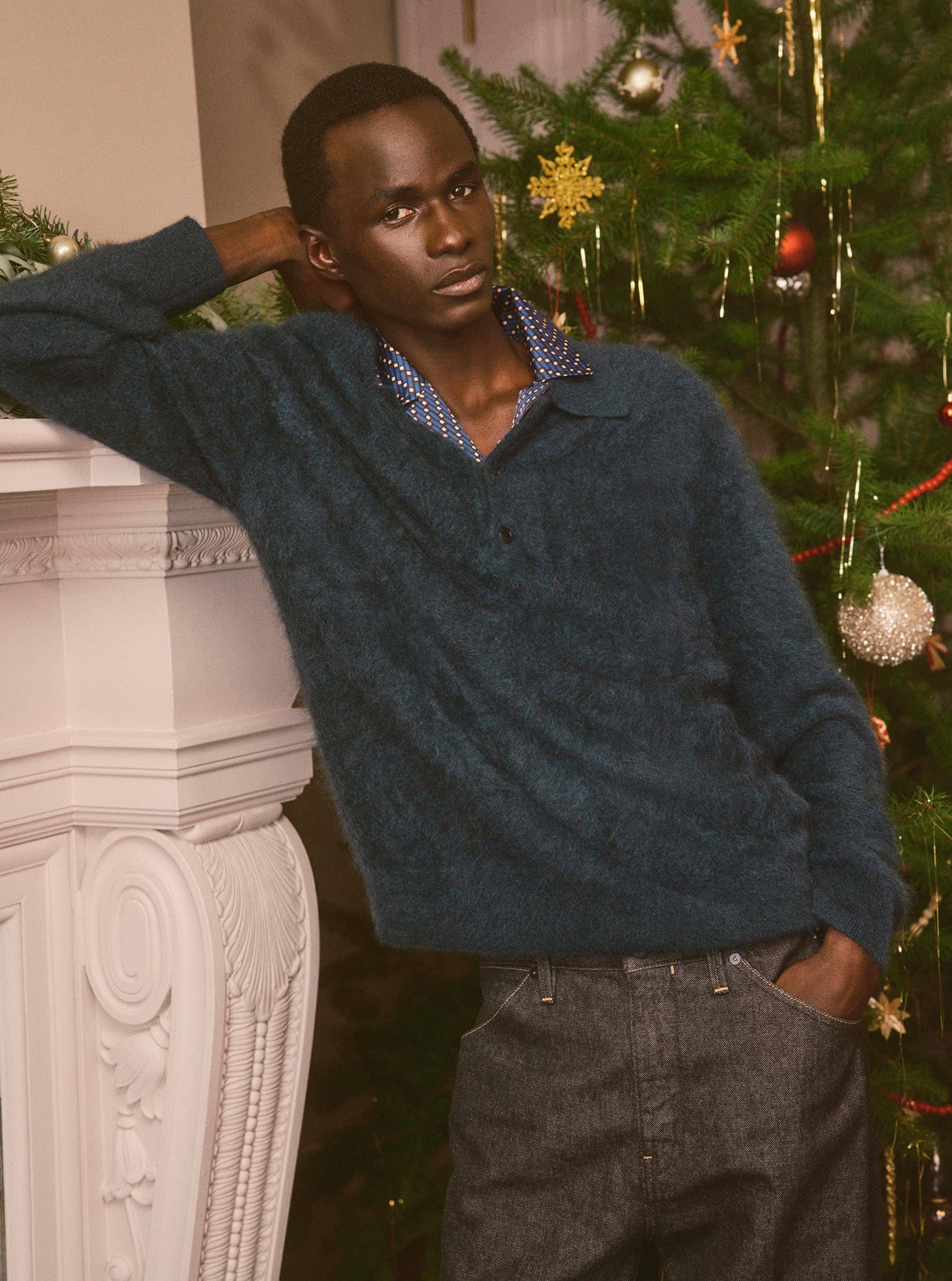 Man leaning against a white fireplace mantel next to a decorated Christmas tree for Banana Republic Holiday 2024 campaign