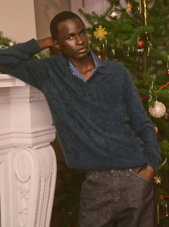 Man leaning against a white fireplace mantel next to a decorated Christmas tree for Banana Republic Holiday 2024 campaign