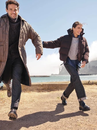 Two smiling models running outdoors near a coastal waterfront wearing winter coats and dark trousers for Banana Republic.