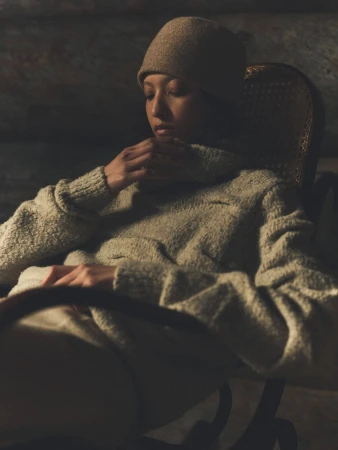 Model wearing a cozy knit turtleneck sweater and beanie sitting in a rustic wooden armchair