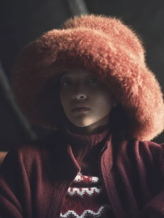Model wearing a fuzzy rust-colored winter hat and matching knitwear for the Loro Piana Après Ski campaign.