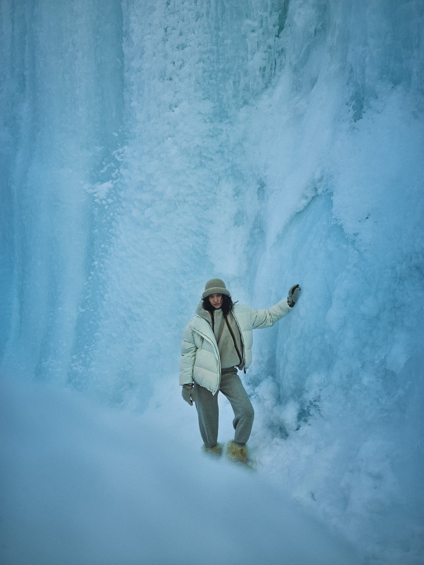 Woman in winter outerwear posing against a massive vertical wall of blue ice and snow formations