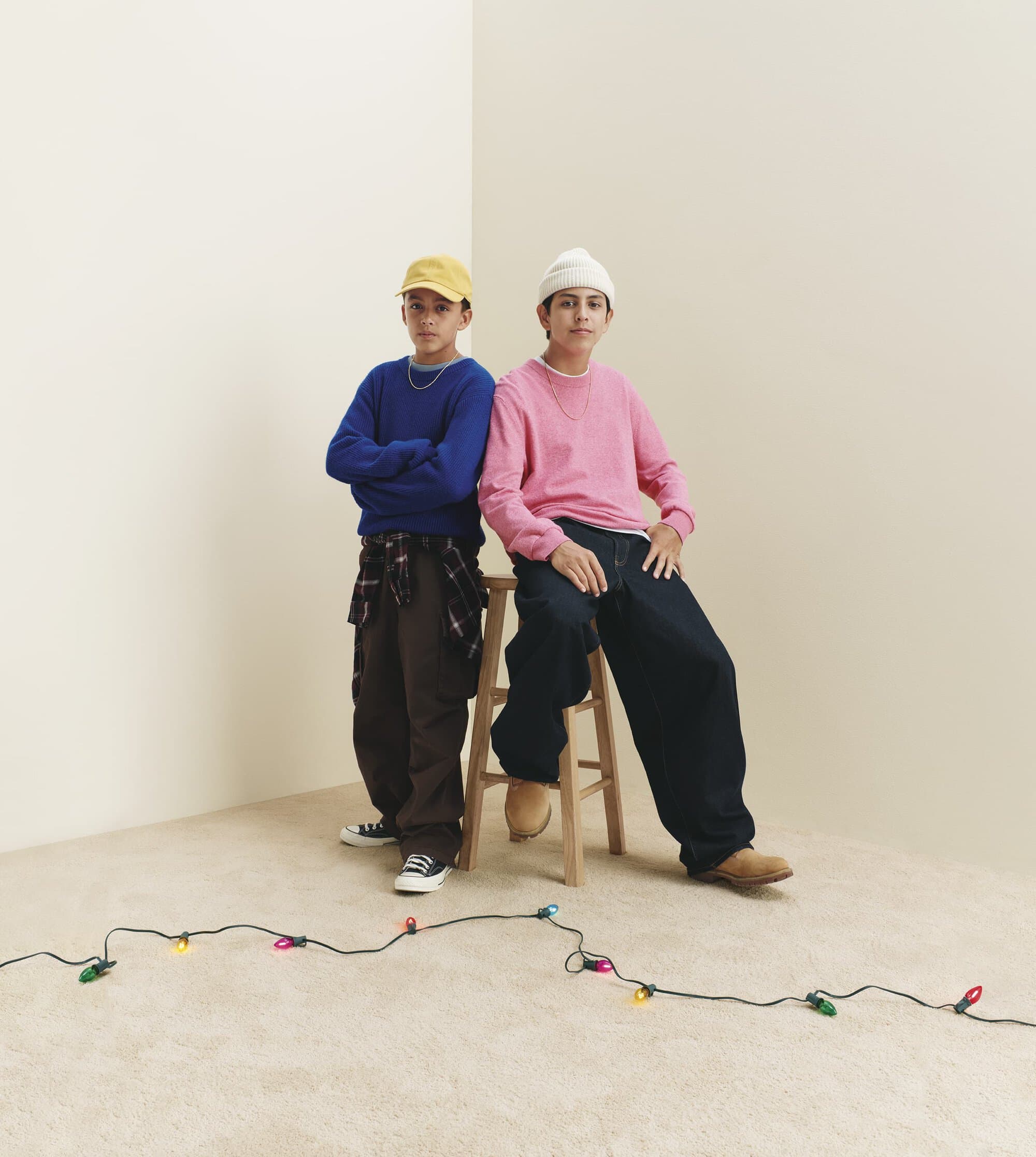 Two boys posing against a neutral corner backdrop with a string of holiday lights on the floor for Gap Holiday 2024 ad campaign.