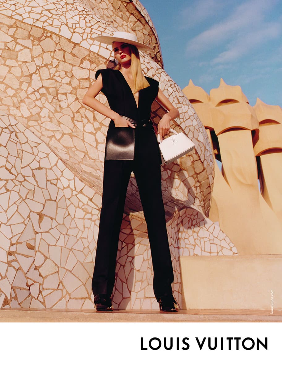 Model wearing a black jumpsuit and white sun hat standing before mosaic stonework for Louis Vuitton Cruise 2025.