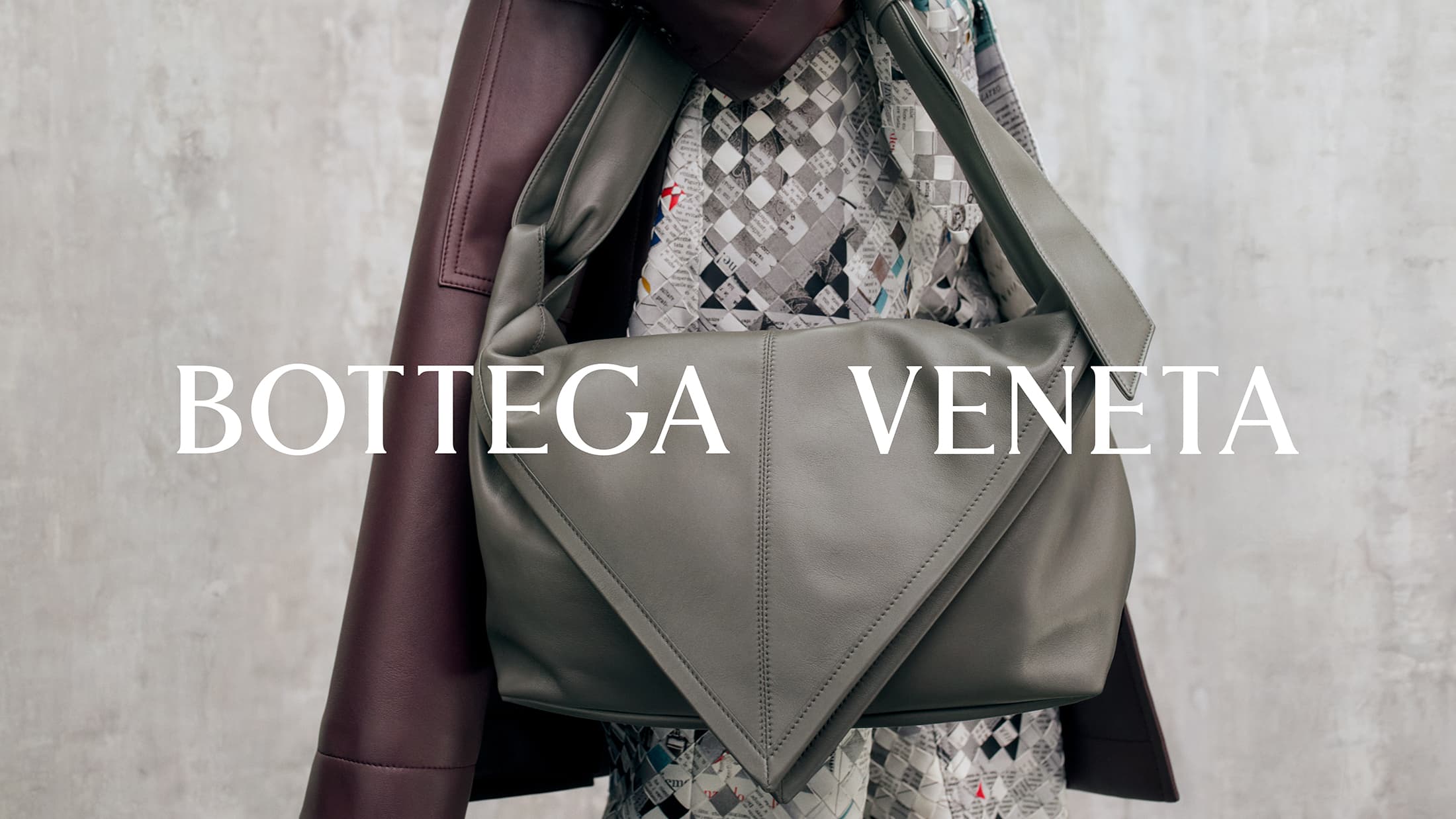 Sage green leather shoulder bag worn against a textured grey concrete wall and dark coat