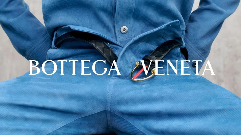 Close-up of a blue suede outfit paired with a black woven leather belt featuring a gold horseshoe buckle