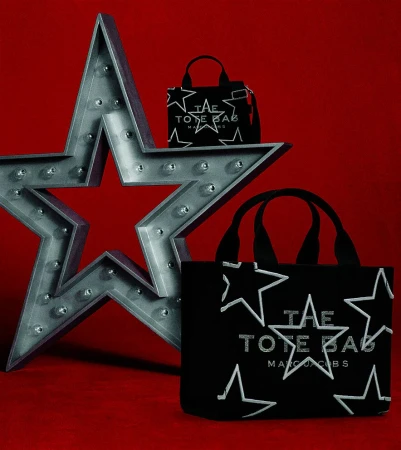 Marc Jacobs tote bags with star patterns displayed next to a large lit star prop on a red background