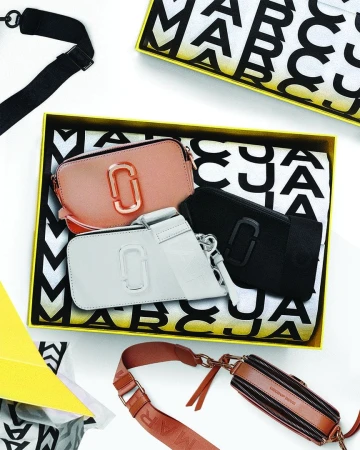 Three Marc Jacobs snapshot leather crossbody bags arranged inside a yellow-edged branded gift box with patterned tissue paper.