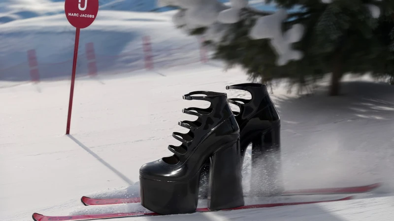 Glossy black platform high-heel shoes mounted on skis speeding down a bright snowfield