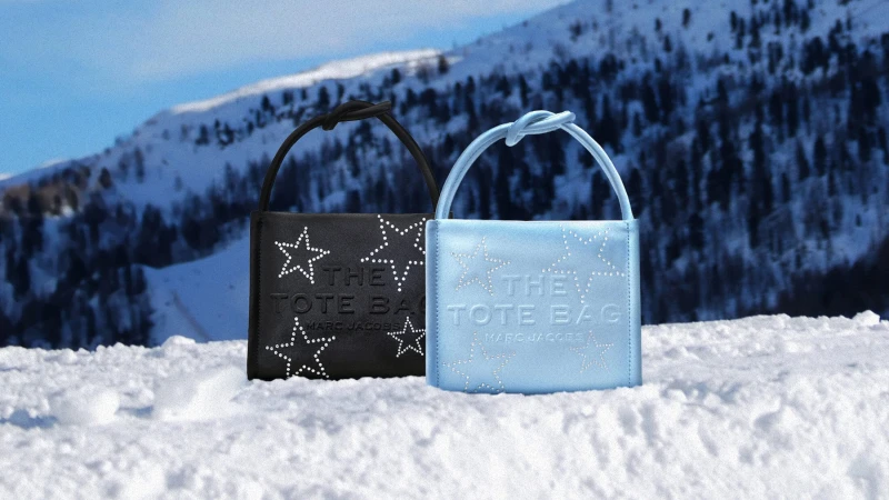 Two Marc Jacobs tote bags embellished with rhinestones resting in snow against a mountain background