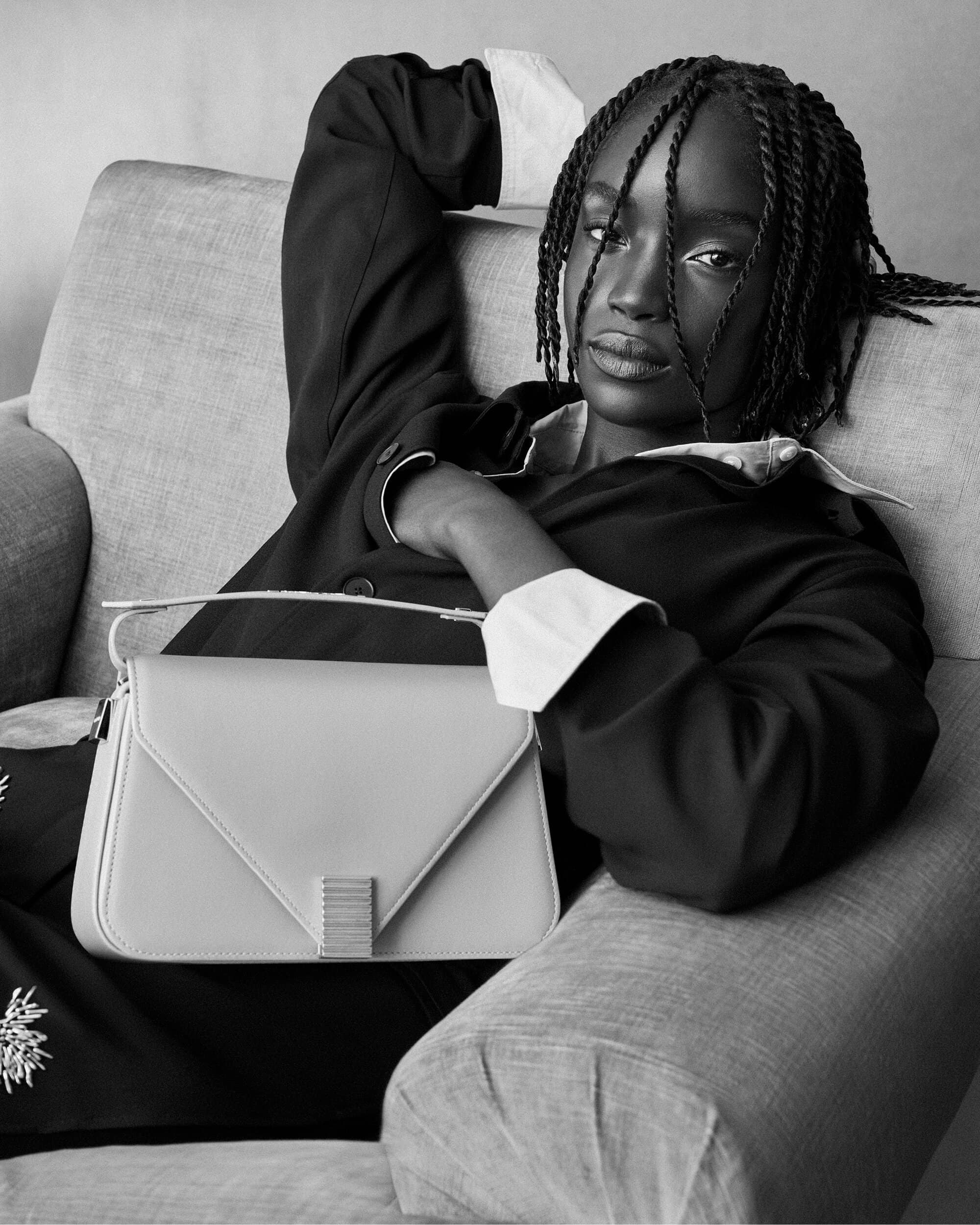 Black woman with braided hair reclining on a sofa holding a light handbag for Lanvin Spring 2025 ad campaign.
