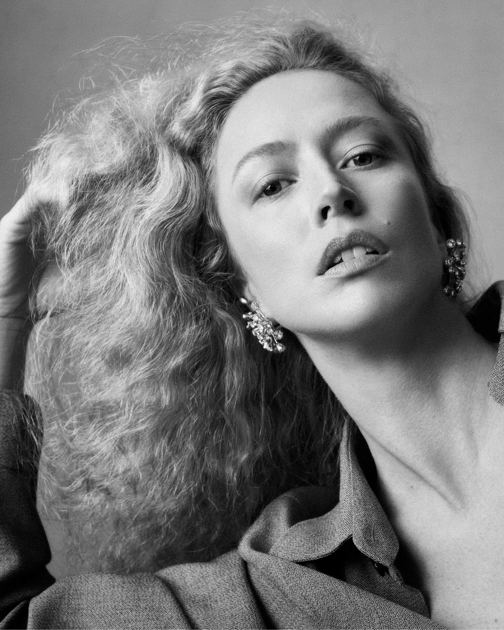 Black and white portrait of a woman with voluminous textured hair holding her hand up to her hair, wearing statement earrings.