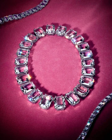 Close-up product shot of sparkling crystal necklaces arranged in a circle on a rich dark pink textured background.